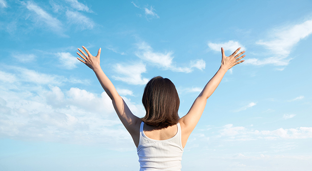 Asian woman holding her hands up against the blue sky